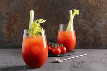 Glasses of bloody mary with celery and tomatoes on grey table