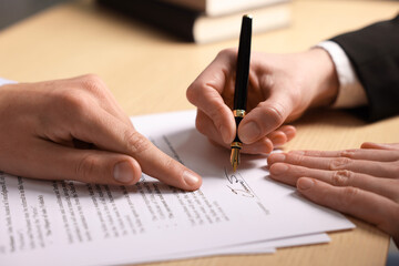 Man pointing at document and woman putting signature at table, closeup