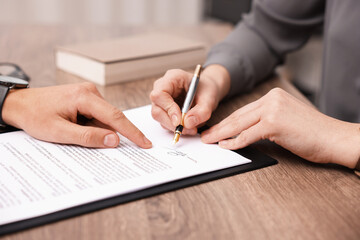 Man pointing at document and woman putting signature at wooden table, closeup