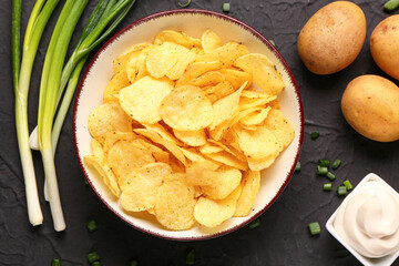 Bowl of tasty sour cream with green onion and potato chips on black background