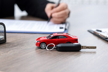 Man signing purchase agreement at wooden table, focus on car model and key. Buying auto