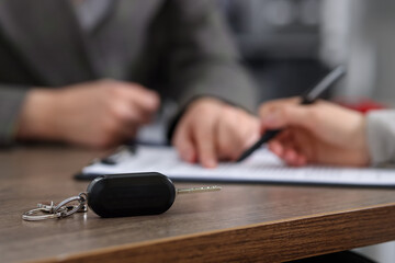 Manager and client signing car purchase agreement at wooden table, selective focus. Buying auto