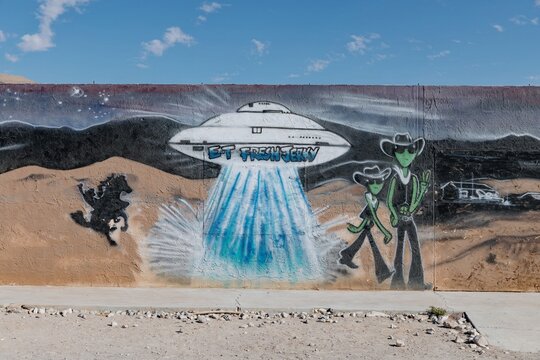 A mural in Nevada depicts aliens and a UFO. The artwork is on a wall with mountains in the background. The mural attracts tourists interested in aliens. Hiko, Nevada, USA. 10 October 2024