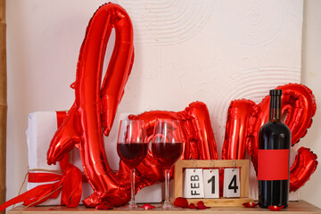 Bottle and glasses of wine, balloon and calendar on dresser at home. Valentine's Day celebration