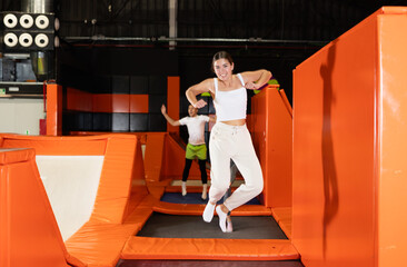 Excited young girl in activewear captured mid-air during fun jump at colorful indoor trampoline...