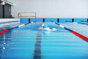 Young man in cap and goggles swimming in pool indoors