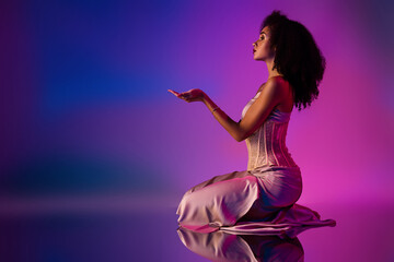 Sensual young woman in a stylish dress posing gracefully under vibrant neon lighting on a colorful background