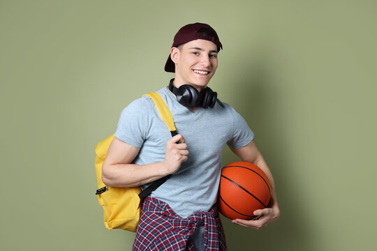 Student with headphones, basketball ball and backpack on olive background - Powered by Adobe