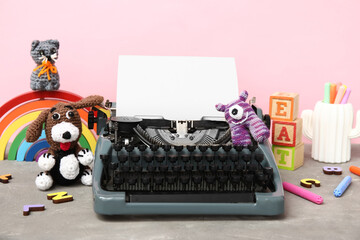 Cute composition with vintage typewriter and knitted toys on table near pink wall