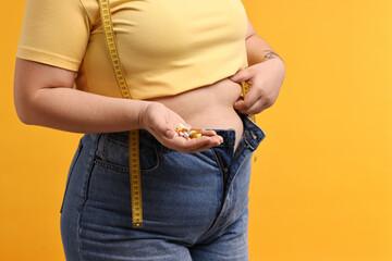 Plus size woman with pile of weight loss supplements on orange background, closeup