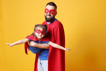 Father and his cute little daughter wearing superhero costumes on orange background