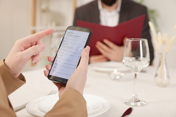 Woman viewing menu on smartphone at table in restaurant, closeup