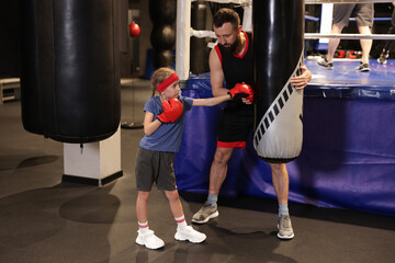Girl in protective gloves having boxing practice with her coach at training center