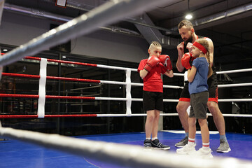 Children practicing fight on boxing ring under their coach supervision. Space for text