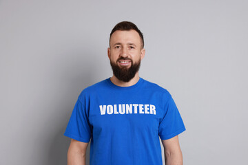 Obraz premium Positive man wearing t-shirt with word Volunteer on light grey background
