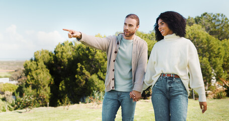 Love, holding hands and pointing with interracial couple in park for relax, date and romance. Happiness, walking and marriage with man and woman in nature for commitment, loyalty and bonding