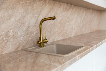 A golden faucet in a modern kitchen with a marble beige facade.