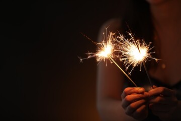 Woman with bright burning sparklers on dark background, closeup. Space for text