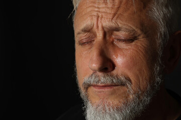Obraz premium Sad senior man crying on black background, closeup. Space for text