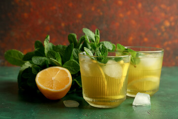 Glasses of tasty lemonade with cut lemon and mint on green grunge table