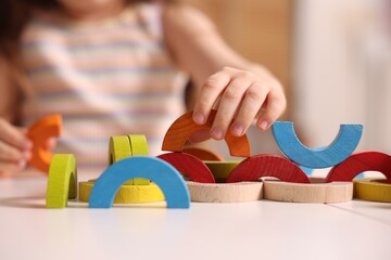 Motor skills development. Little girl playing with colorful wooden pieces at white table indoors,...