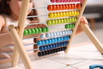 Motor skills development. Little girl playing with wooden abacus at table indoors, closeup