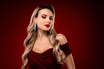 Fototapeta premium Glamorous young woman in a stylish red dress with long blonde hair against a burgundy background