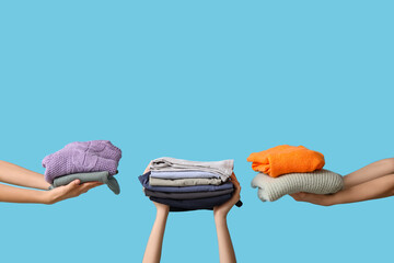 Many female hands with stacks of different clothes on blue background