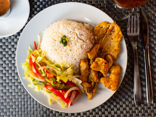 Appetizing spicy roasted chicken breast served with side dish of fluffy white rice, and fresh vegetable salad. Traditional Latin American dish