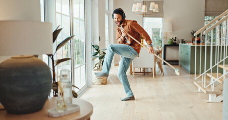 Energy, music and sweeping with man in home for chores, responsibility or spring cleaning. Broom, dance and headphones with excited person in apartment for housekeeping, listening or radio streaming
