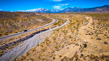 Aerial of Desert Road with Black Car and Snow-Capped Mountains