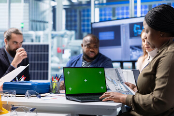 Factory management team look over schematics, planning work using isolated screen laptop. Solar panels plant shareholders look over assembly lines blueprints diagrams, working on mockup notebook