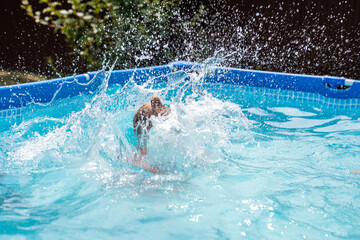 Child making a big splash in a backyard pool on a sunny day, caught in motion