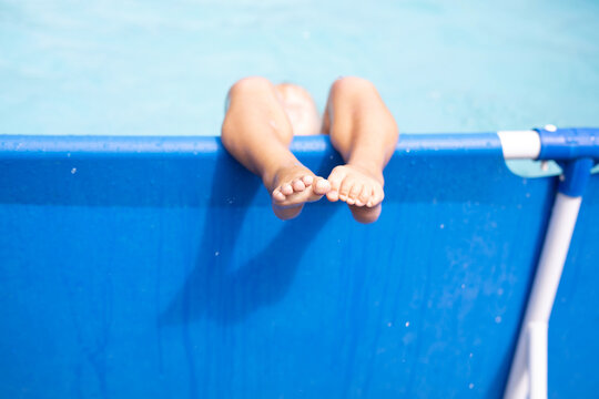 Bare feet of a small child resting on the edge of an inflatable pool on a sunny day