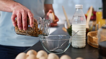 Man hands pouring cornflakes at bowl in cozy home closeup. Brunette adding milk