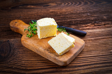 Fresh French sea salt butter garnished with thyme offered as close-up on a rustic wooden chopping board