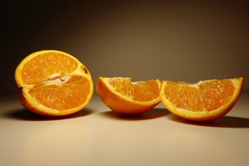 Fresh orange cut into halves and wedges placed on a neutral surface. Juicy citrus fruit displayed under soft studio lighting. Healthy eating, vitamin C, and natural food concept