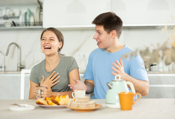 Happy young couple sitting at the kitchen-table and having a warm conversation while drinking tea