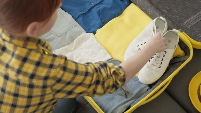 A diligent person packs a yellow suitcase with clothes, shoes, and a camera, demonstrating organization for an exciting adventure and a hasslefree trip filled with unforgettable experiences