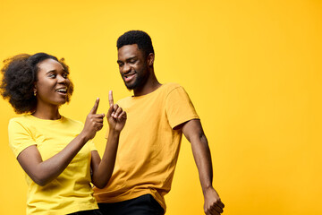 Obraz premium Happy African couple having fun and dancing against a bright yellow background, wearing casual yellow and black clothes, expressing joy and connection