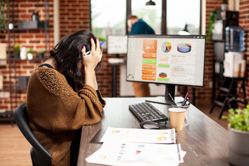 Female analyst resting her head in hands, showing exhaustion from office workload. Tired white...