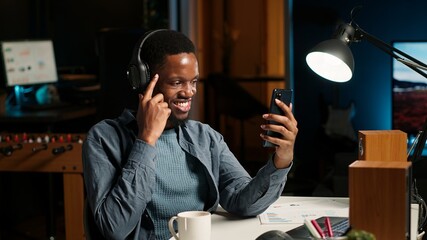 African american man waving and attending a web meeting from his urban apartment. Engaged male...