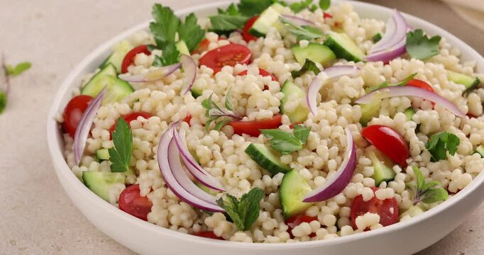 Pearl couscous salad with red onion, herbs and tomatoes, close up, camera rotates around