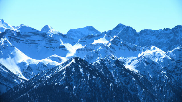Snow-covered mountains rise majestically under a clear blue sky during a sunny winter day in a remote alpine region