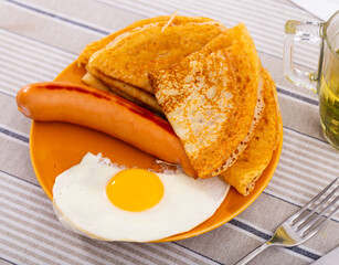 Grilled meat sausage with pancakes and fried egg on a plate side view