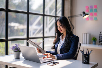 Fototapeta premium A woman in a business suit is sitting at a desk with a laptop and a book