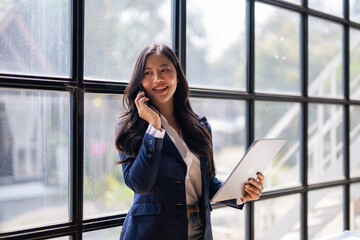 A woman in a business suit is talking on her cell phone while holding a tablet