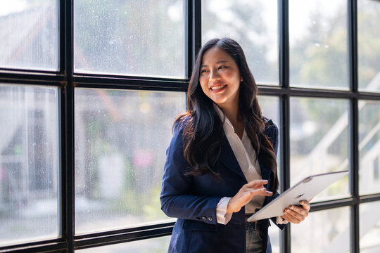 A woman in a business suit is smiling and holding a tablet