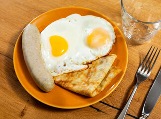 Fried egg, golden pancakes and chicken sausage - hearty snack, homemade village breakfast. Hot herbal tea is served with meal.