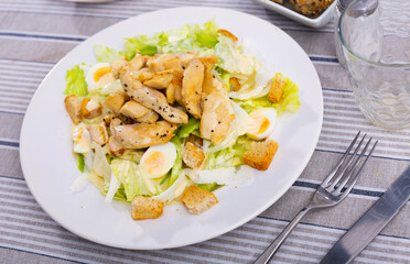 Traditional Caesar salad recipe - fried chicken fillet pieces with romaine lettuce leaves and wheat croutons, seasoned with cheese sauce and supplemented with quail eggs